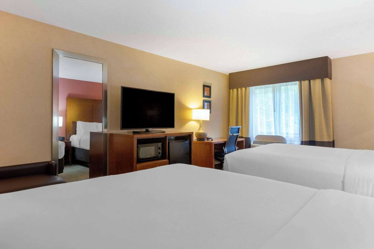 A hotel room with two beds, a television, a desk with a lamp, a microwave, and a small refrigerator.