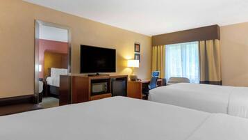 A hotel room with two beds, a television, a desk with a lamp, a microwave, and a small refrigerator.
