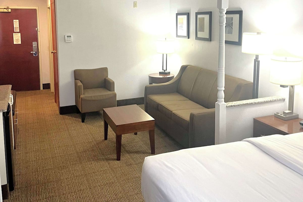A hotel room with a bed, a sofa, a chair, a small table, and two bedside lamps.