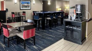 A hotel lobby with a bar area, seating with red and grey cushions, a coffee machine, and a clock on the wall. - Comfort Inn & Suites Jackson North (Jackson)