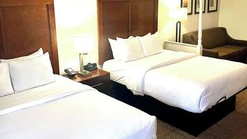 Une chambre d’hôtel avec deux lits simples, une table de chevet avec une lampe, un téléphone et un fauteuil brun.