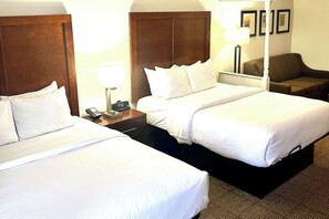 A hotel room with two single beds, a nightstand with a lamp, a telephone, and a brown armchair.