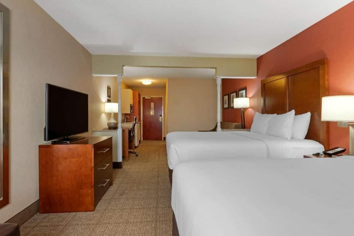 A hotel room with two beds, a TV, a desk, and a lamp.