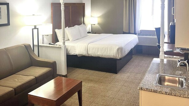 A hotel room with a bed, a sofa, a coffee table, a desk, a lamp, a sink, and a window with curtains. - Comfort Inn & Suites Jackson North (Jackson)