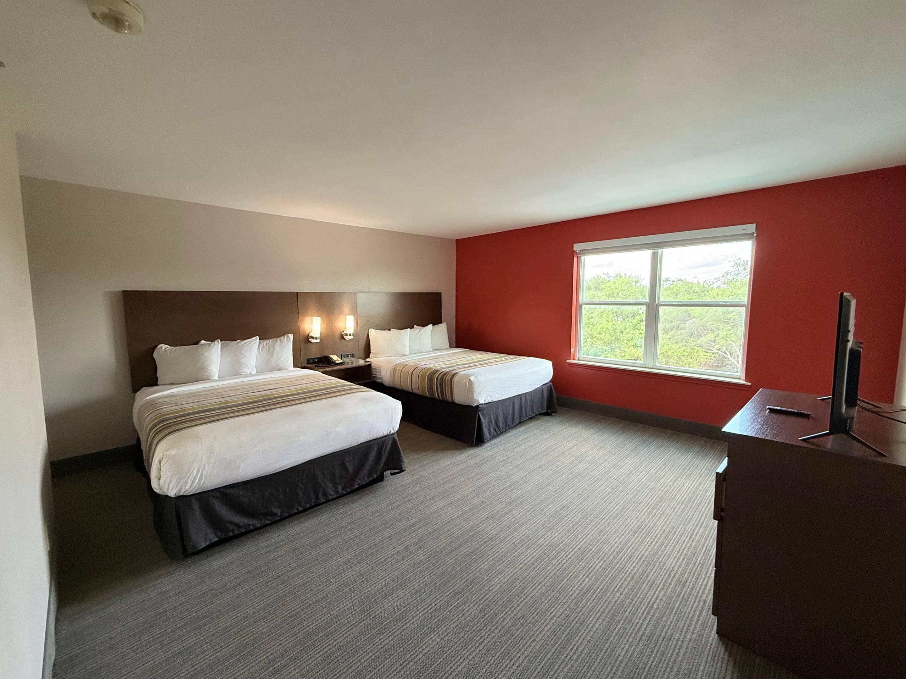 A hotel room with two beds, a large window, and a desk with a TV.