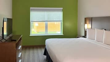 Una habitación de hotel con una cama grande, un televisor sobre un tocador de madera, una ventana con persianas y una mesita de noche con una lámpara.