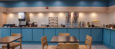 A restaurant with blue walls, wooden tables and chairs, and a counter with various food items and condiments.