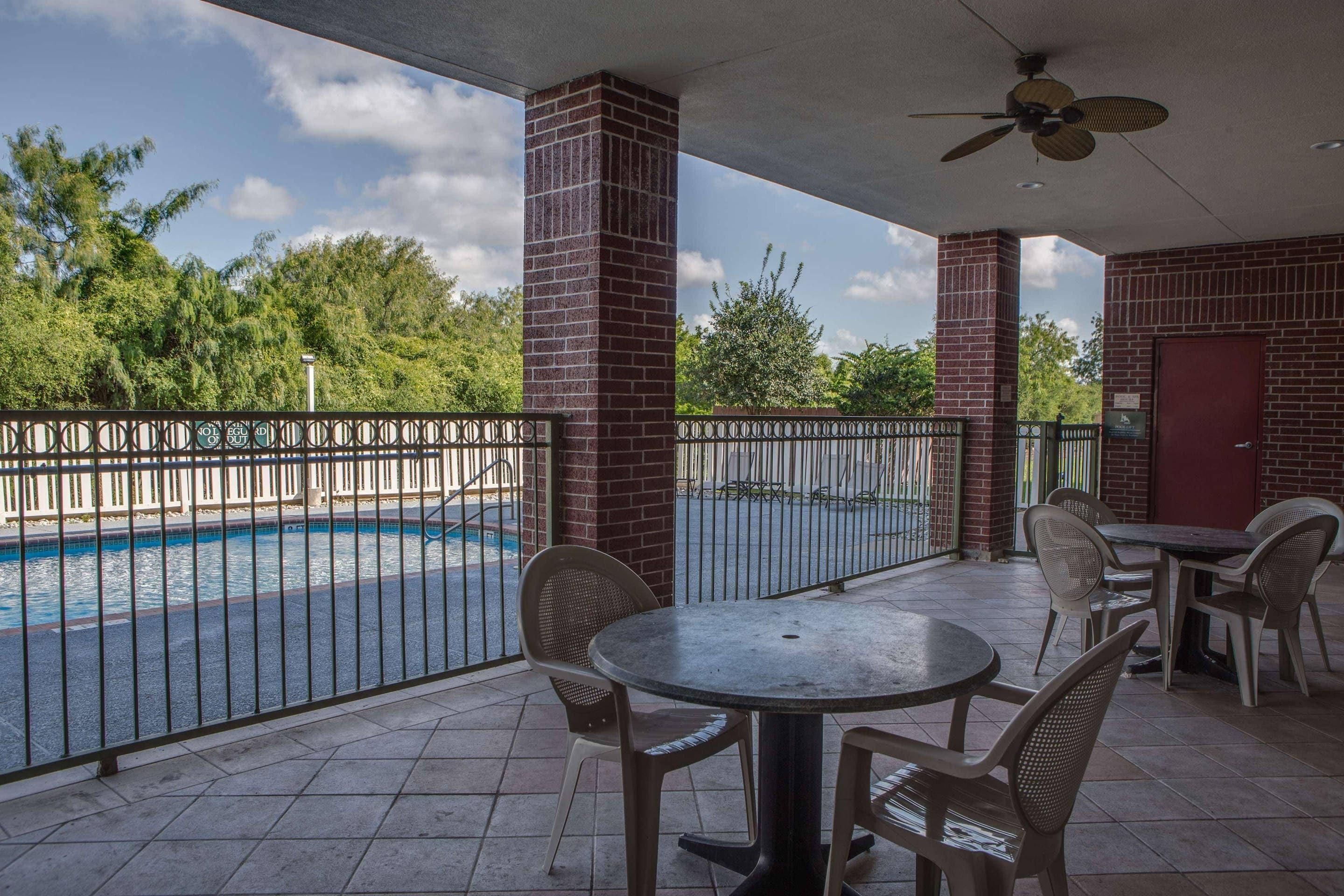 An outdoor patio with a pool, brick pillars, and a ceiling fan.