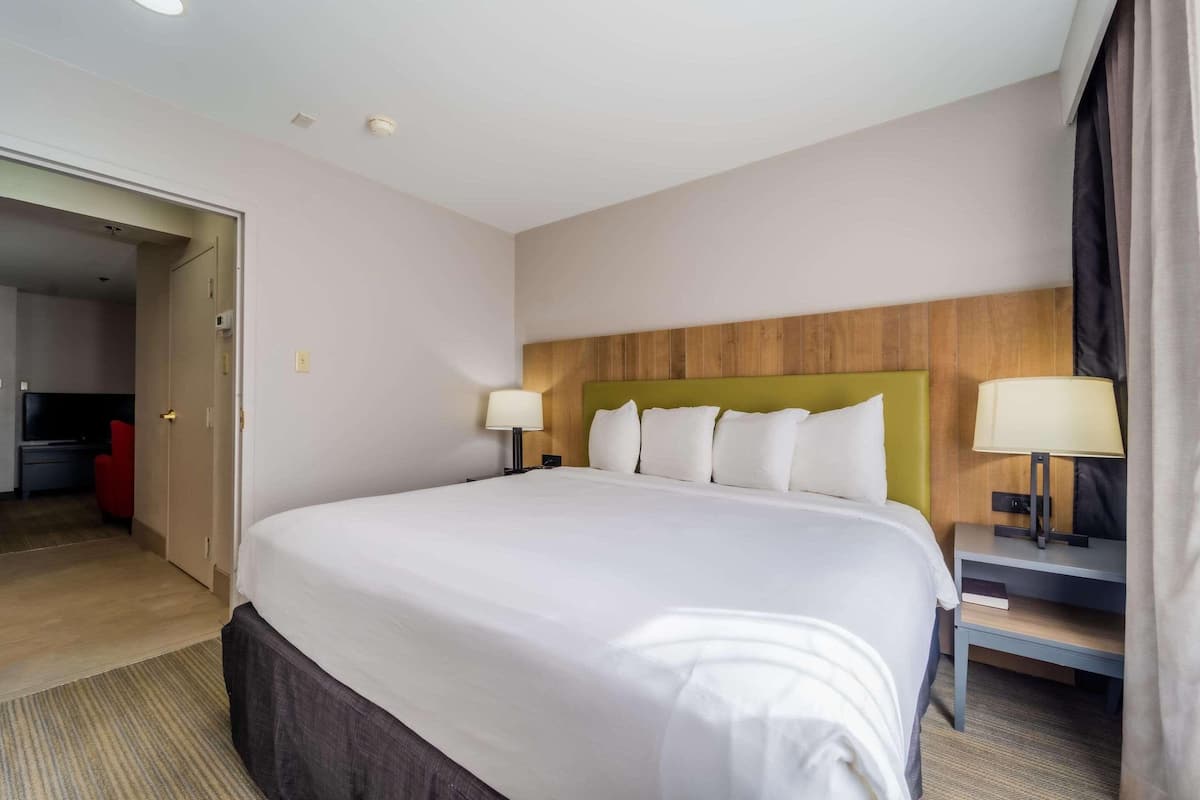 A hotel room with a large bed, two bedside tables with lamps, a wooden headboard, and a door leading to another room.