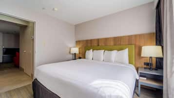 Habitación de hotel con una cama grande, dos mesitas de noche con lámparas, un cabecero de madera y una puerta que da a otra habitación.