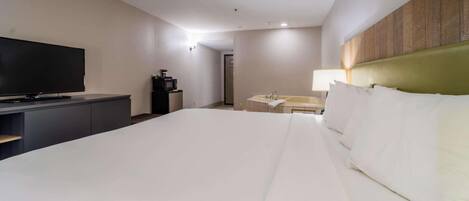 Habitación de hotel con una cama grande, un televisor de pantalla plana, un escritorio con ordenador y un baño con lavabo y espejo.