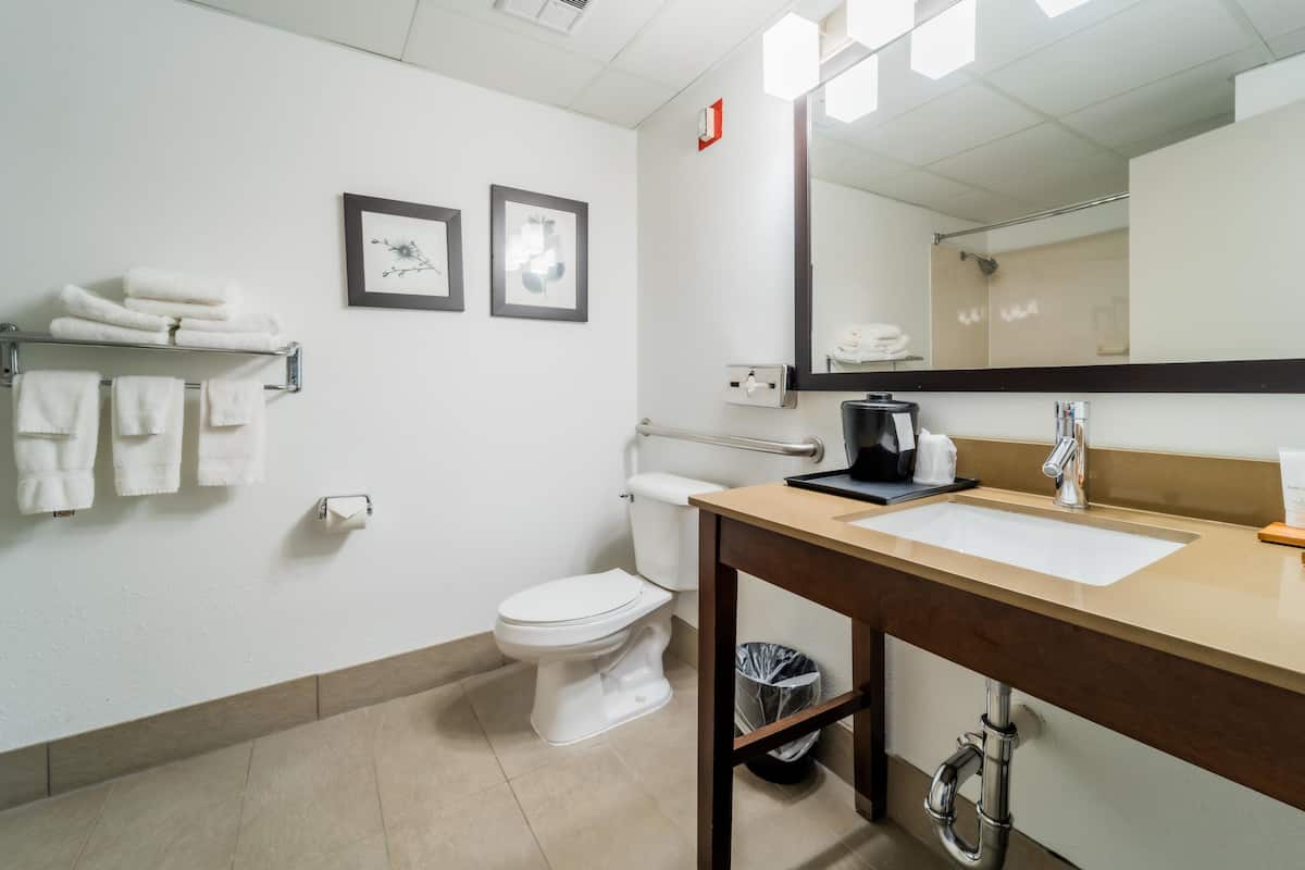 A modern bathroom with a white toilet, a sink with a mirror above it, and a towel rack with folded towels.