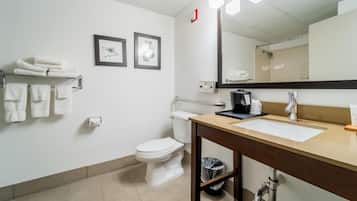 Une salle de bain moderne avec des toilettes blanches, un lavabo surmonté d’un miroir et un porte-serviettes avec des serviettes pliées.