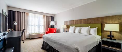 A hotel room with a large bed, a desk, a chair, and a TV.