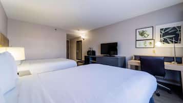 A hotel room with two beds, a desk, a chair, a television, and framed botanical artwork on the wall.