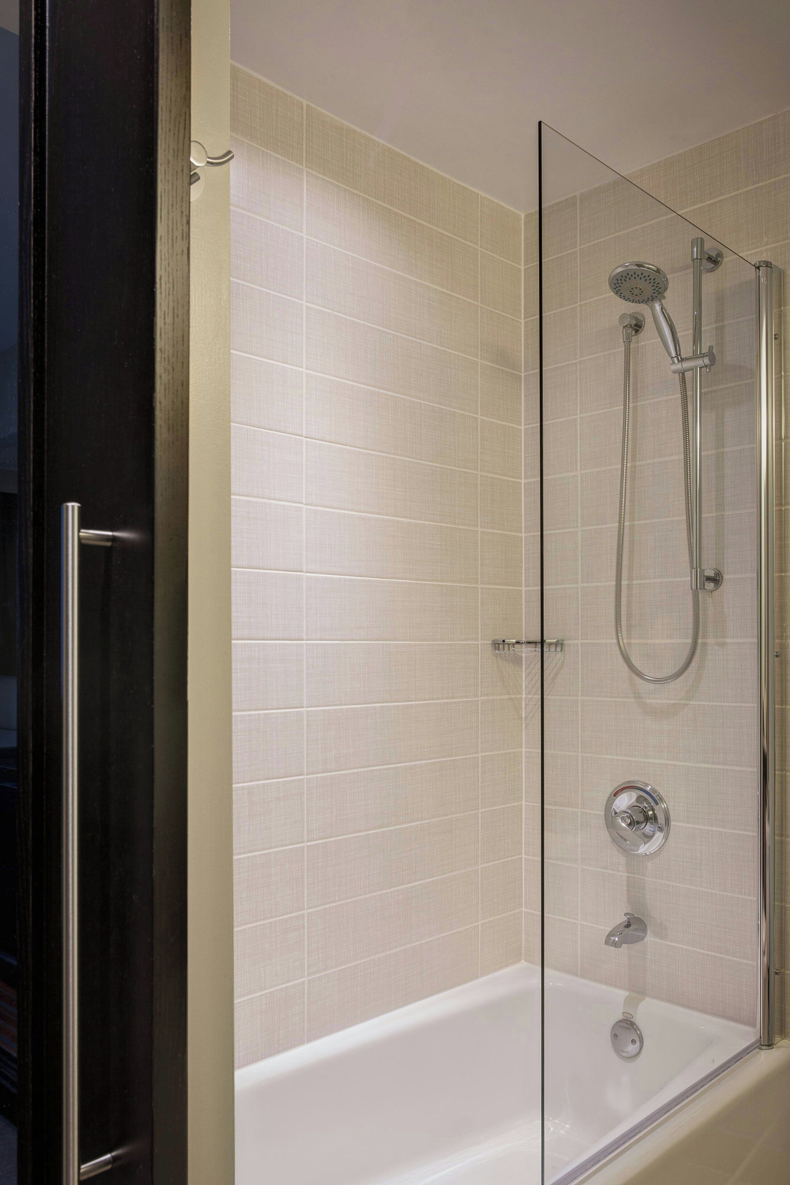 A glass-enclosed shower with a handheld showerhead and a handheld faucet.