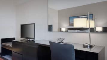 A modern hotel room with a desk, a flat-screen TV, a telephone, and a lamp.