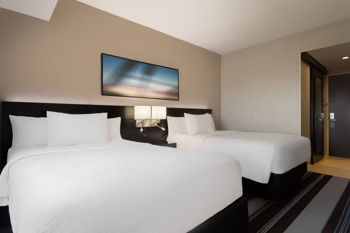 A hotel room with two beds, a nightstand, a lamp, and a painting on the wall.