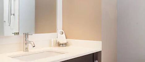 A bathroom with a sink, mirror, towel rack, and toilet paper dispenser.