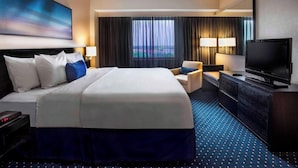 A hotel room with a large bed, a television, a desk, and a view of the cityscape through the window.