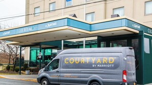 A gray van with 'Courtyard by Marriott' branding parked in front of a hotel entrance. - Courtyard by Marriott New York JFK Airport (Jamaica)