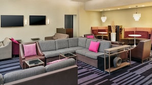 A modern hotel lobby with a sectional sofa, armchairs, a small table, and a flat-screen TV mounted on the wall.