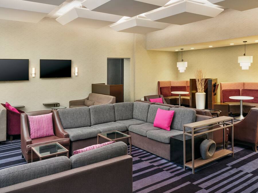 Eine moderne Hotelhalle mit Ecksofa, Sesseln, einem kleinen Tisch und einem an der Wand befestigten Flachbildfernseher.