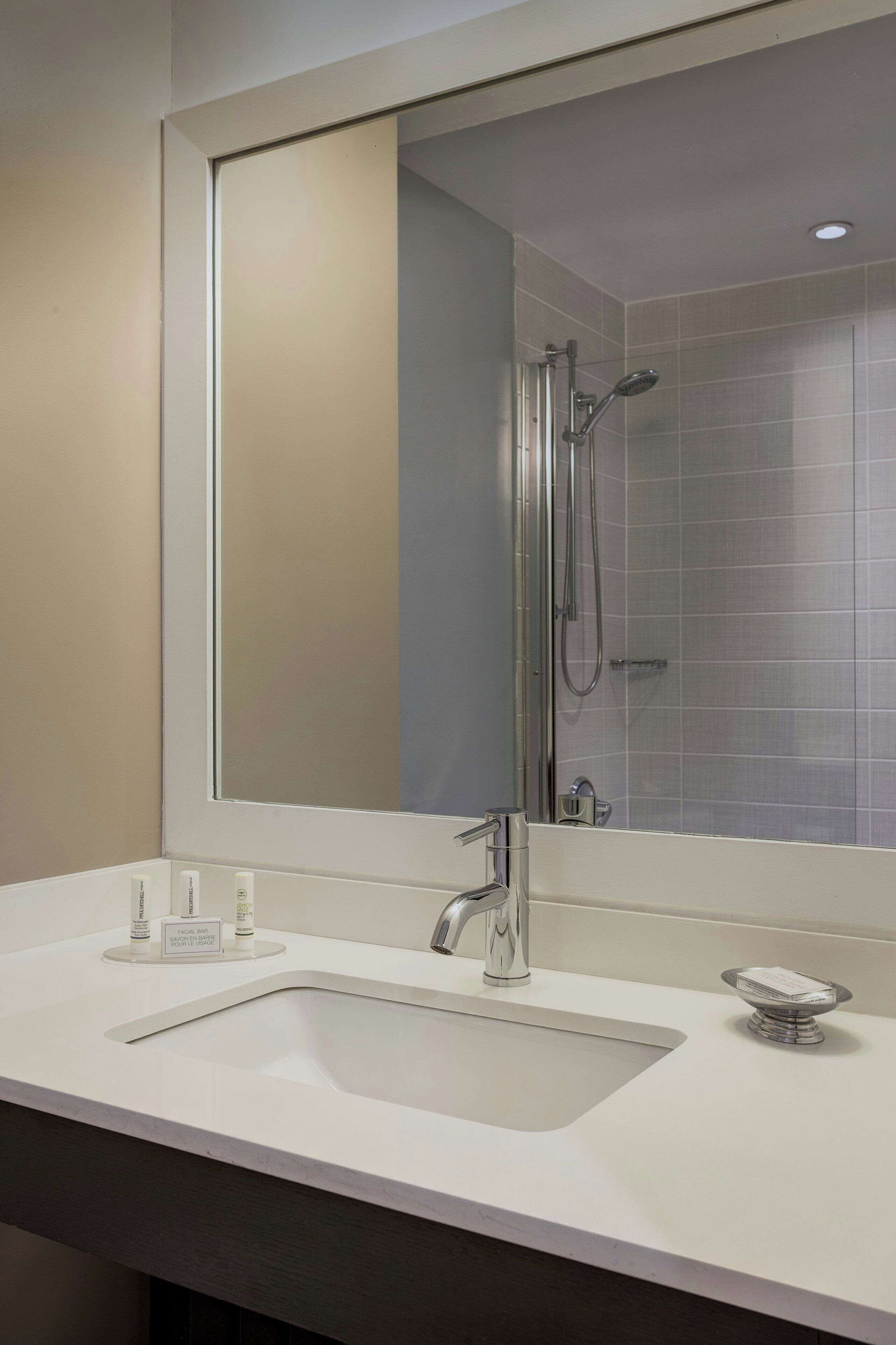 A modern bathroom with a large mirror, a sink, and a shower.