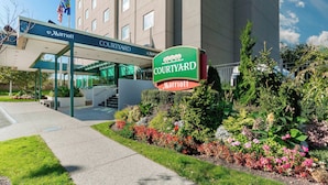 A Marriott Courtyard hotel entrance with a covered walkway, a sign, and landscaped gardens.