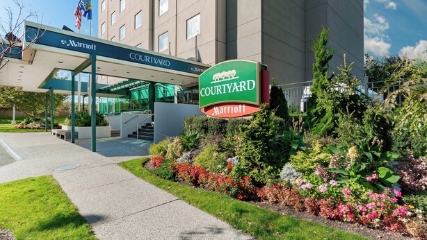 A Marriott Courtyard hotel entrance with a covered walkway, a sign, and landscaped gardens. - Courtyard by Marriott New York JFK Airport (Jamaica)