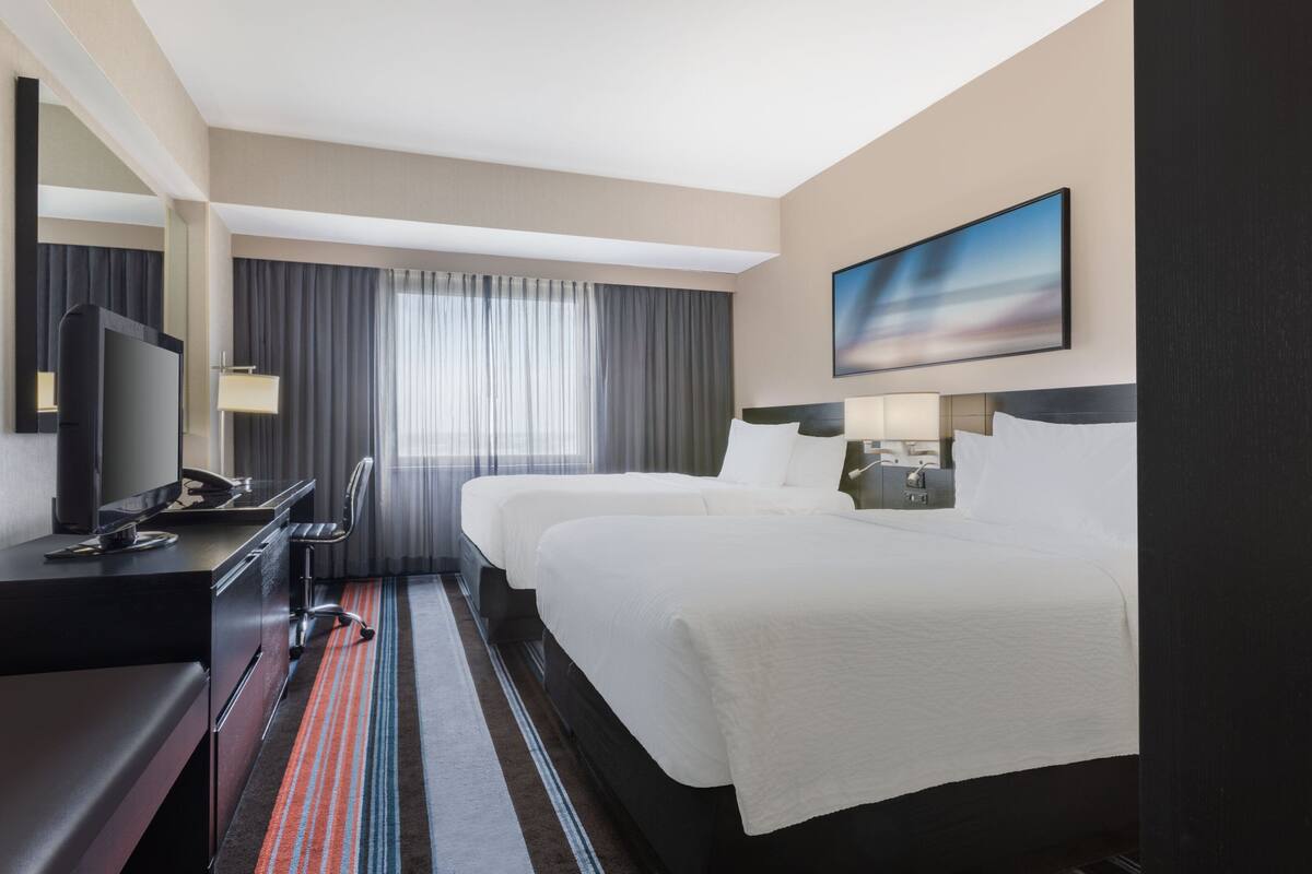 A hotel room with a large bed, a desk with a computer, a TV, and a window with curtains.