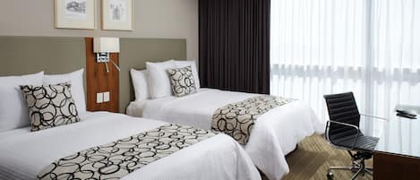 A hotel room with two beds, a desk, and a chair. There are two framed pictures on the wall.