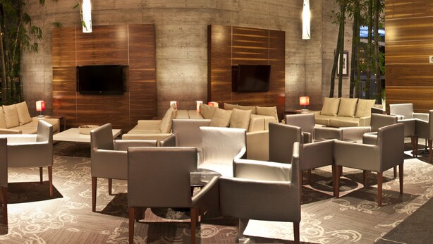 A modern lobby with multiple seating areas, a reception desk, and a large wall-mounted TV. - Casa Inn Premium Hotel Queretaro (El Marques)