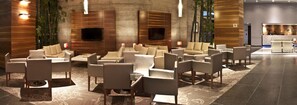 A modern lobby with multiple seating areas, a reception desk, and a large wall-mounted TV. - Casa Inn Premium Hotel Queretaro (El Marques)