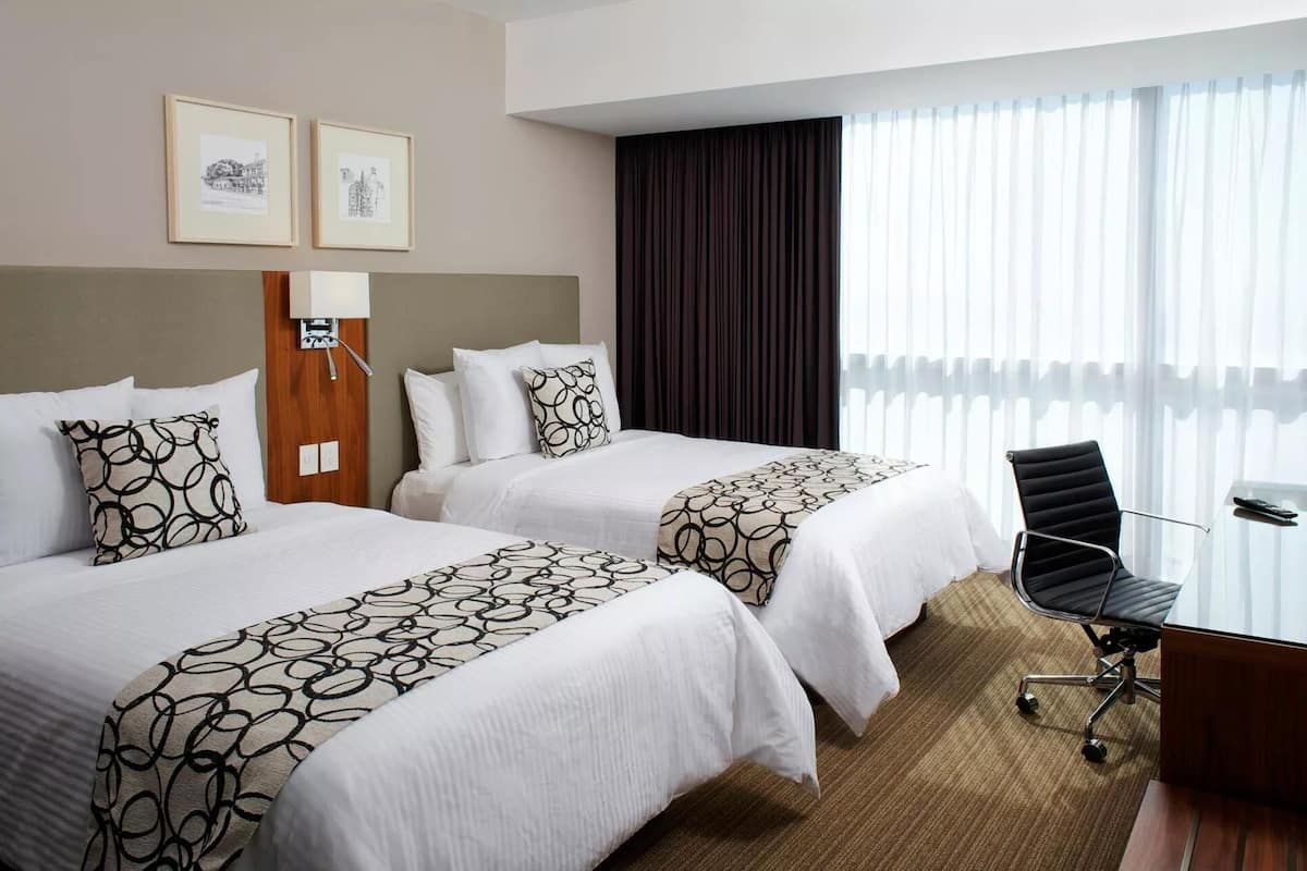 A hotel room with two beds, a desk, and a chair.