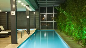 An indoor swimming pool with a glass wall, lounge chairs, and a hot tub. - Casa Inn Premium Hotel Queretaro (El Marques)