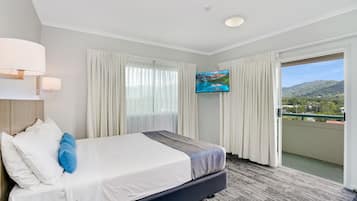 A hotel room with a bed, a TV mounted on the wall, and a balcony with a view of the mountains.