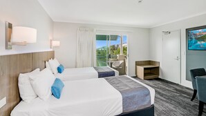 Habitación de hotel con dos camas, un escritorio, una silla, un televisor y un balcón con vistas.
