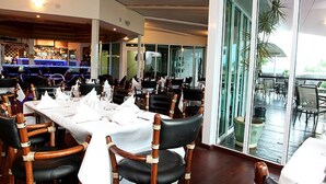 Un restaurante con sillas de madera, manteles blancos y una zona de bar al fondo.