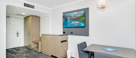 A modern hotel room with a flat-screen TV mounted on the wall, a small table with a chair, and a wooden cabinet.