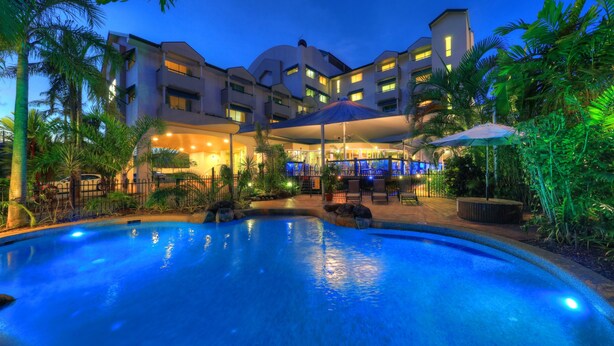 Un hotel con piscina, mobiliario exterior y una zona cubierta con sombrillas.