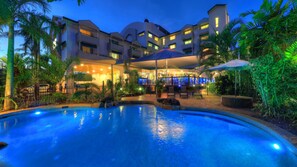 Un hotel con piscina, mobiliario exterior y una zona cubierta con sombrillas.