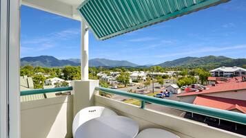 A balcony with a view of mountains, a parking lot, and a building with a red roof.
