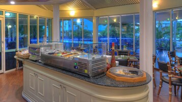 Un área de bufé con una estación de autoservicio, un comedor con mesas y sillas, y ventanas amplias que ofrecen vistas al exterior.