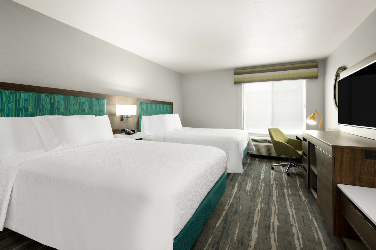 A hotel room with two beds, a desk, a chair, a TV, and a window with a view.