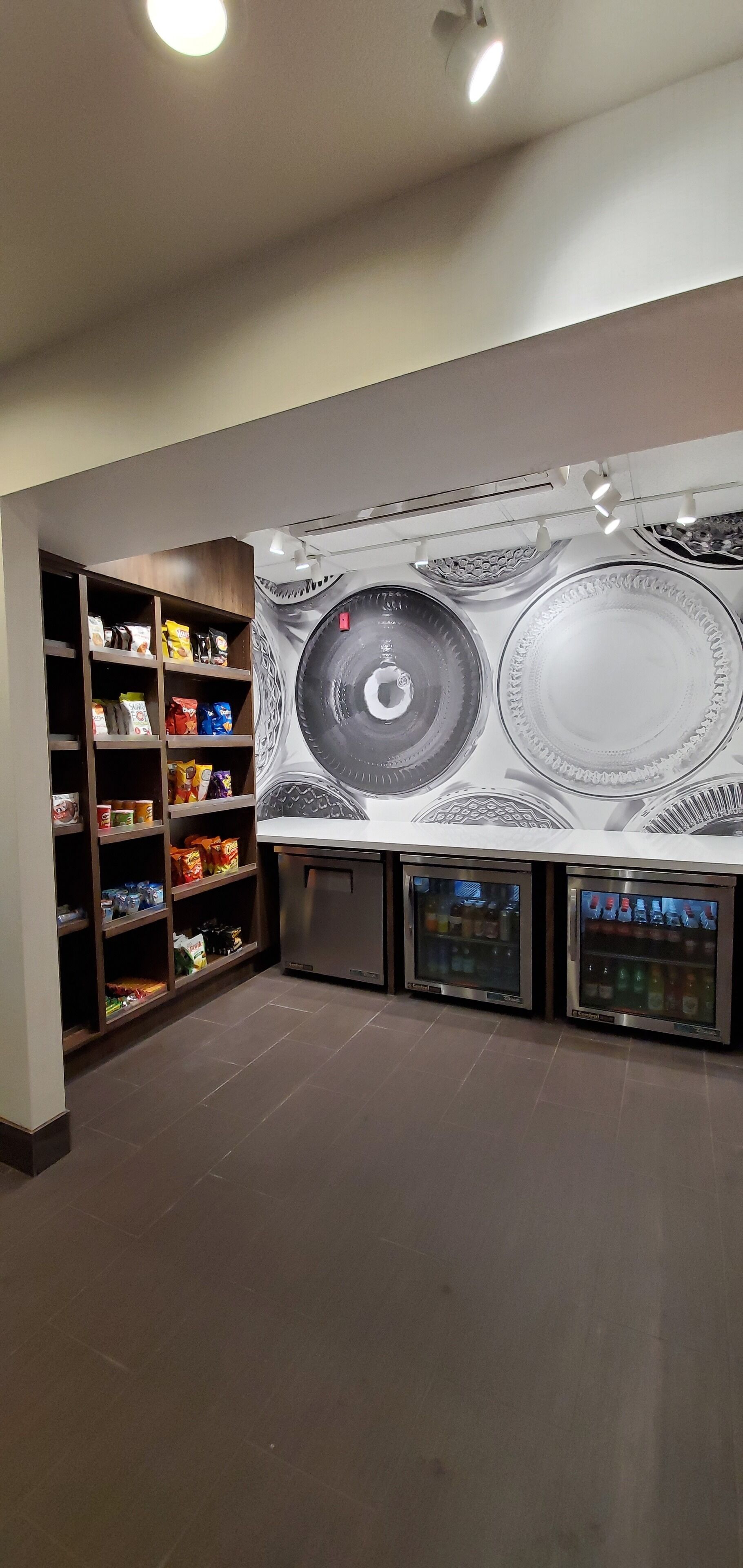 Amplia habitación con un mural grande en la pared, estanterías empotradas llenas de aperitivos y una máquina expendedora.