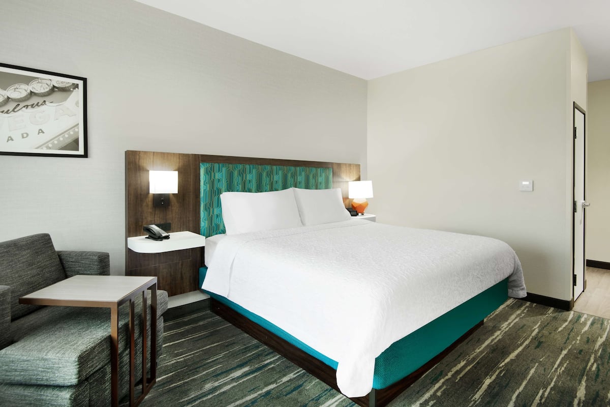 A hotel room with a bed, a small table, a chair, a nightstand, and a wall-mounted phone.