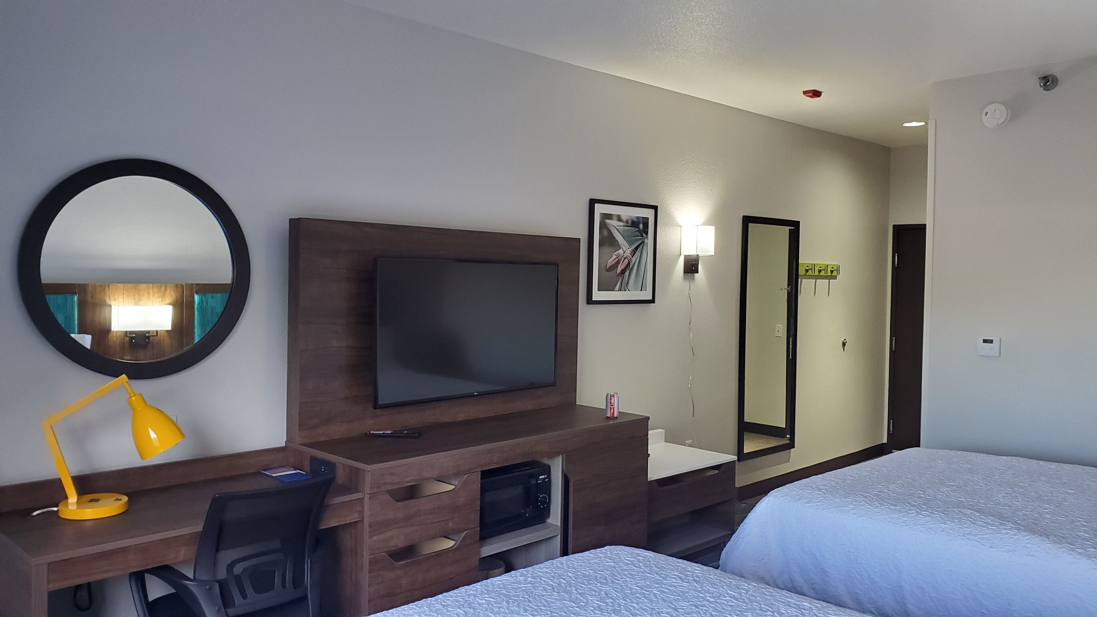 Ett hotellrum med en säng, ett skrivbord med en dator, en tv, en spegel och en badrumsdörr.