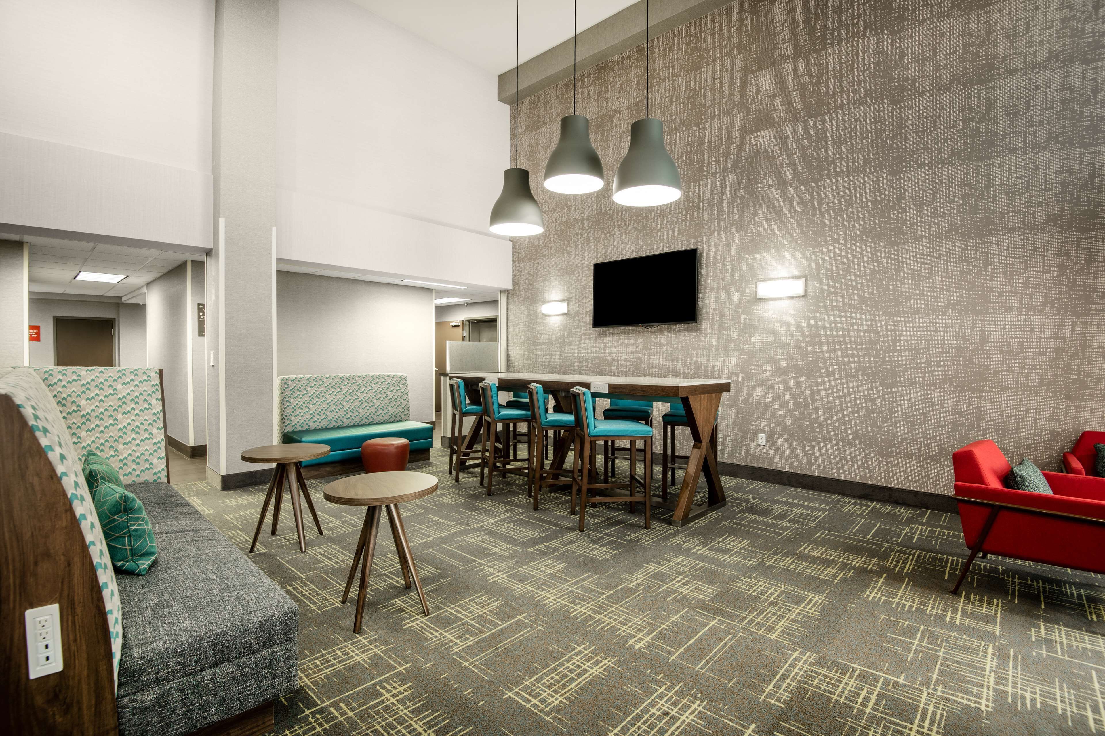 Un hall d’hôtel moderne doté d’un espace salon, d’un bar et d’un téléviseur à écran plat fixé au mur.