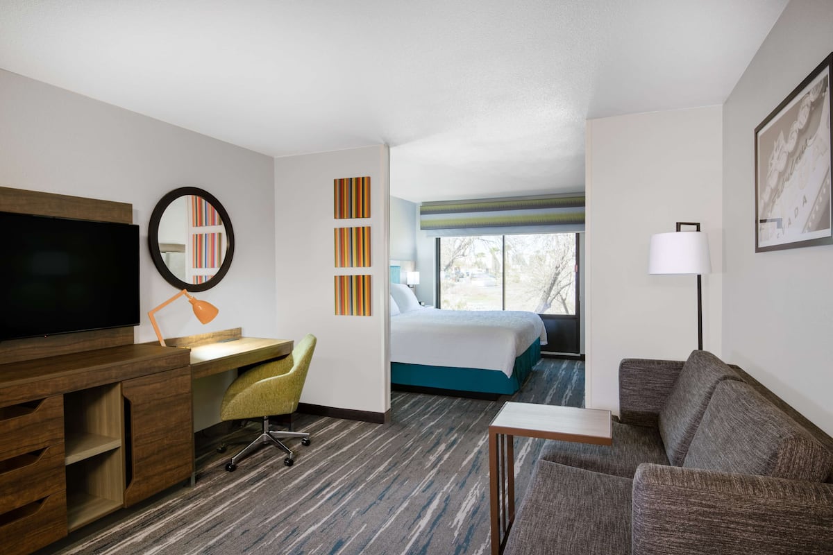 A hotel room with a bed, a desk with a chair, a television, and a couch.